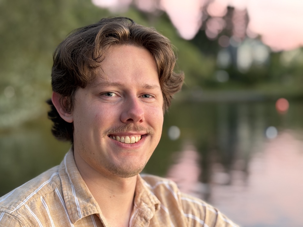 Holland Farr smiling outdoors near a lake at sunset.