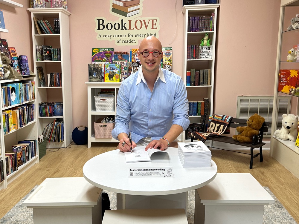 London England smiling while signing a copy of the book Transformational, not Transactional at a bookstore.